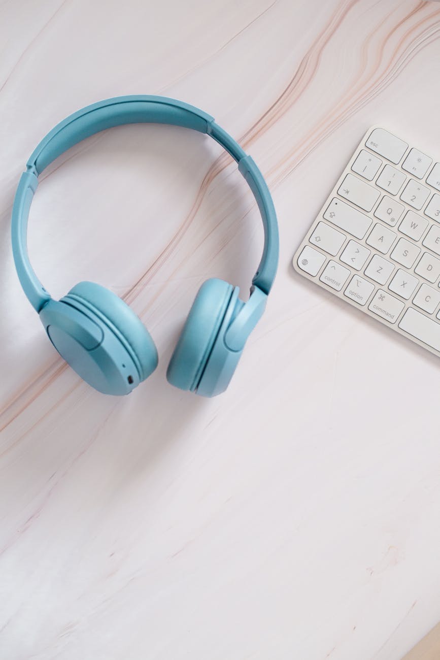 A clean and modern workspace featuring blue headphones and a white keyboard on a smooth surface.