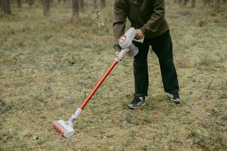 Unusual scene of a person using a vacuum cleaner on grass in the forest.