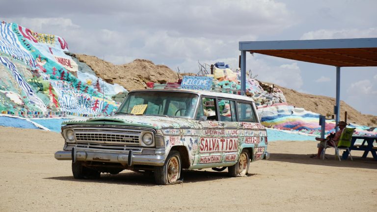 A painted vintage car at Salvation Mountain in Slab City, showcasing vibrant art and desert background.