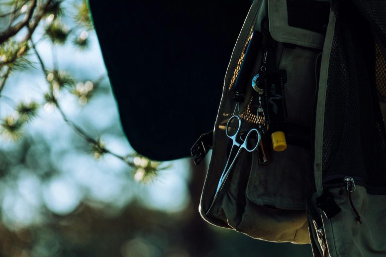 Close-up of a forester vest with tools and scissors outdoors among blurred trees.