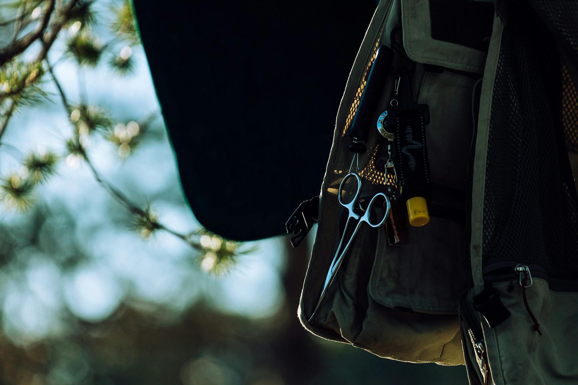 Close-up of a forester vest with tools and scissors outdoors among blurred trees.