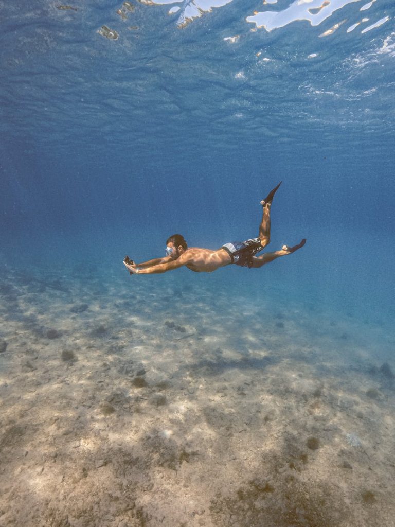 A man free diving underwater over a rocky sea floor in Arraial do Cabo, Brazil.