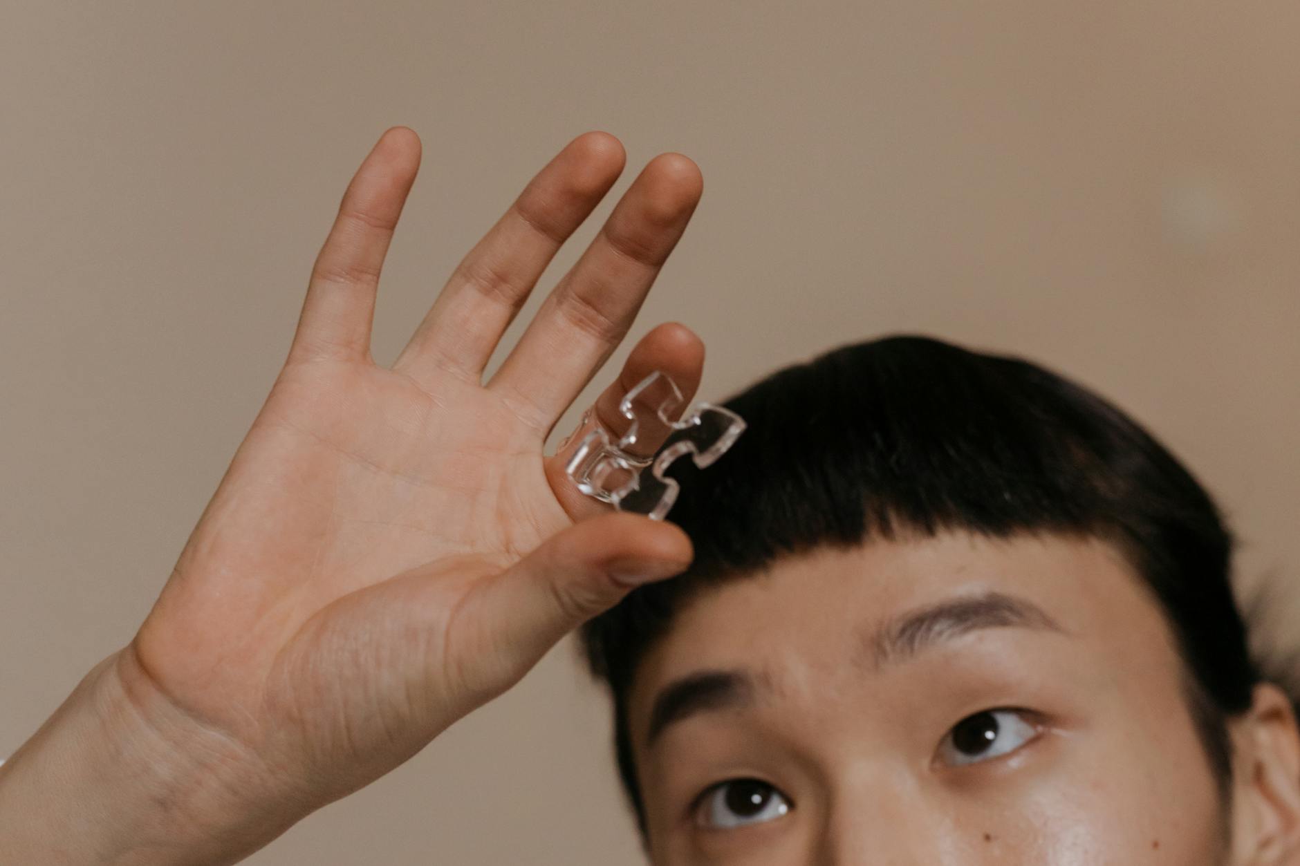 Person holding a transparent puzzle piece, focusing on the hand and expression.