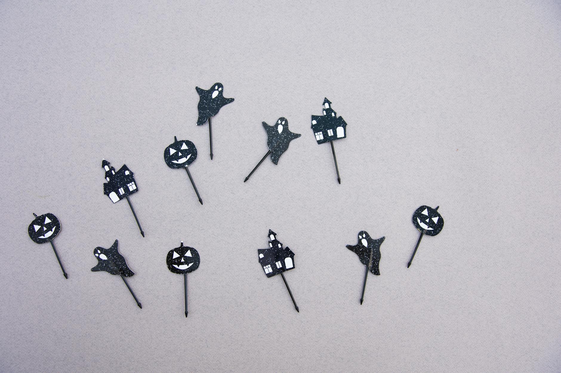 Black ghost and pumpkin cutouts scattered on a light surface perfect for a Halloween party.