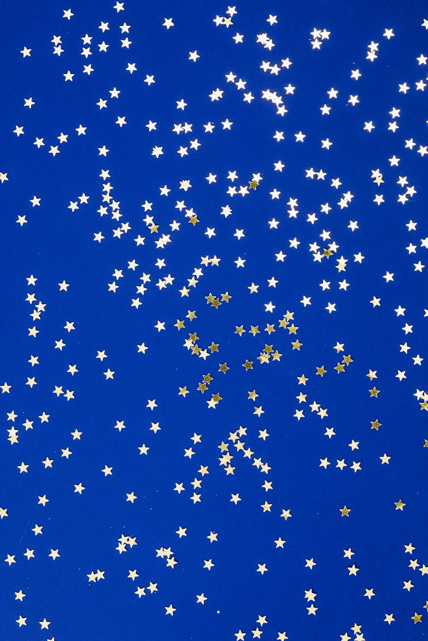 Golden star confetti scattered on a deep blue surface, creating a festive and whimsical pattern.