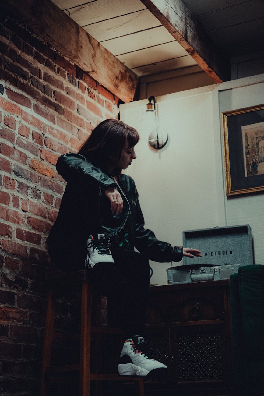 A moody indoor portrait featuring a woman with a vintage vinyl player and exposed brick wall.