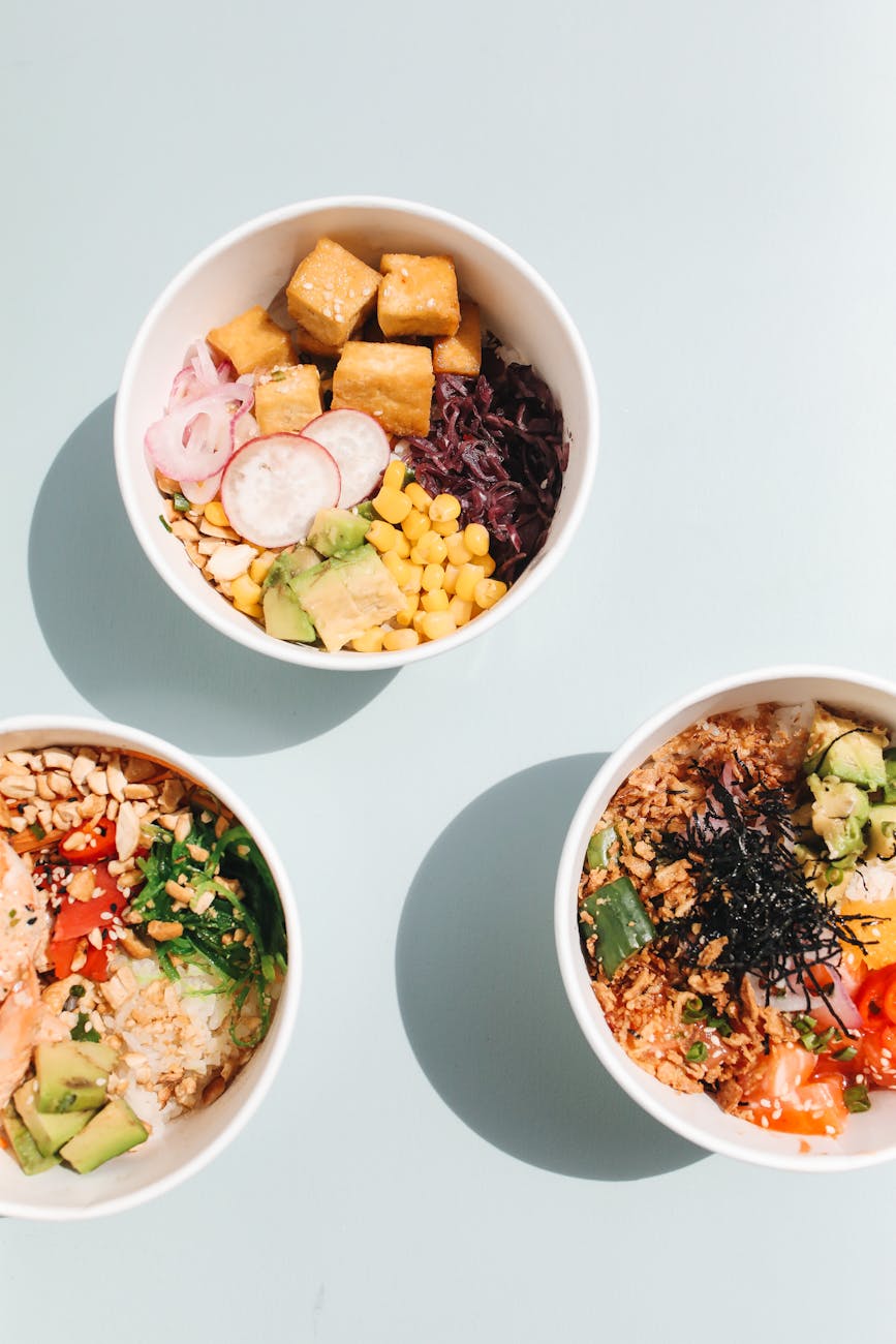 Three colorful poke bowls with fresh ingredients like avocado, corn, and tofu.