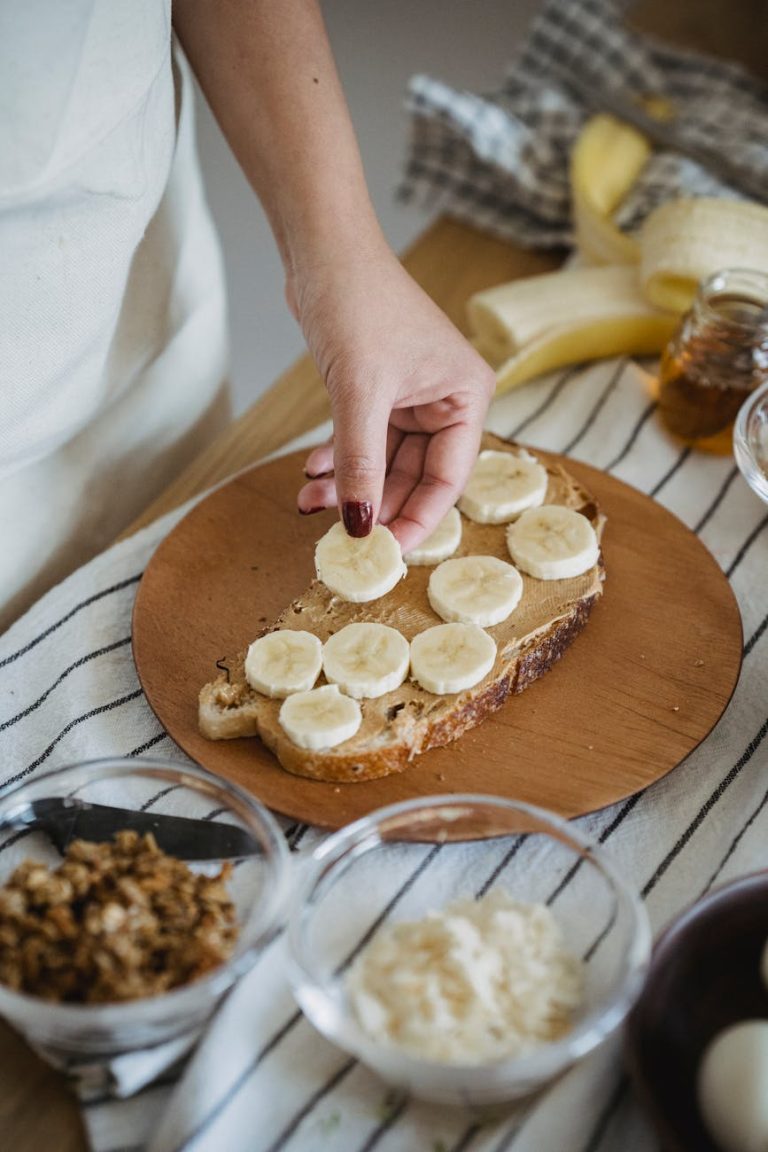 Hand placing banana slices on toasted bread. Perfect healthy breakfast preparation.