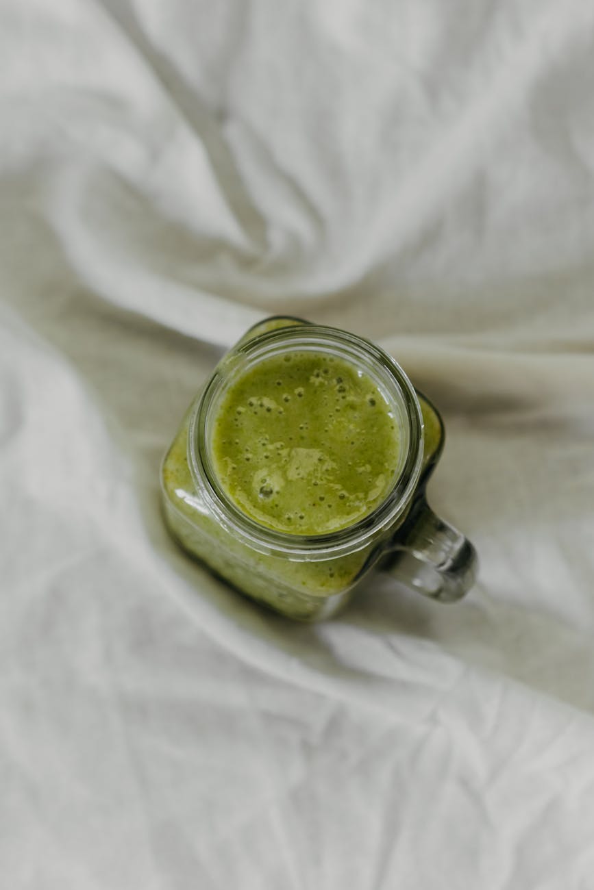 Top view of a nutritious green smoothie in a glass jar on a soft fabric background.