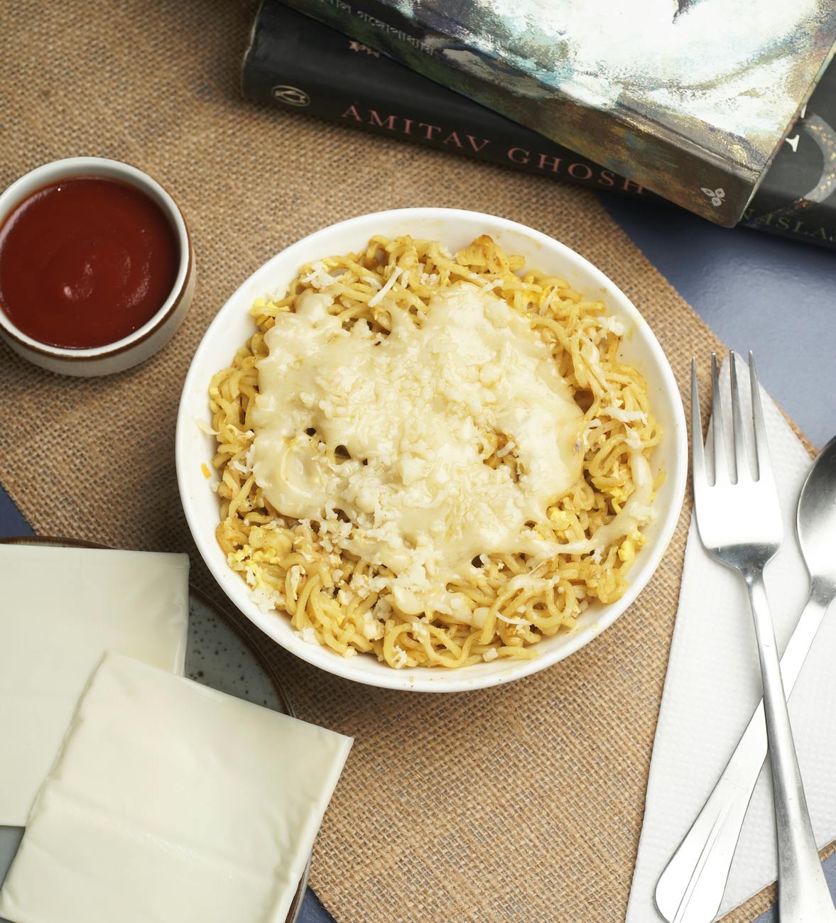 Bowl of golden noodles topped with melted cheese and tomato sauce on the side.