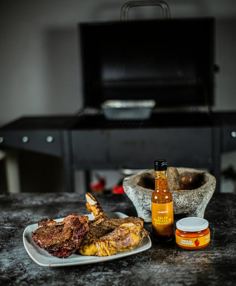 Steak cuts on a plate with spicy sauces and a barbecue grill in the background.