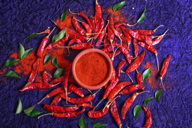 Vibrant red chili peppers and powder arranged on a textured purple background, offering a bold culinary theme.