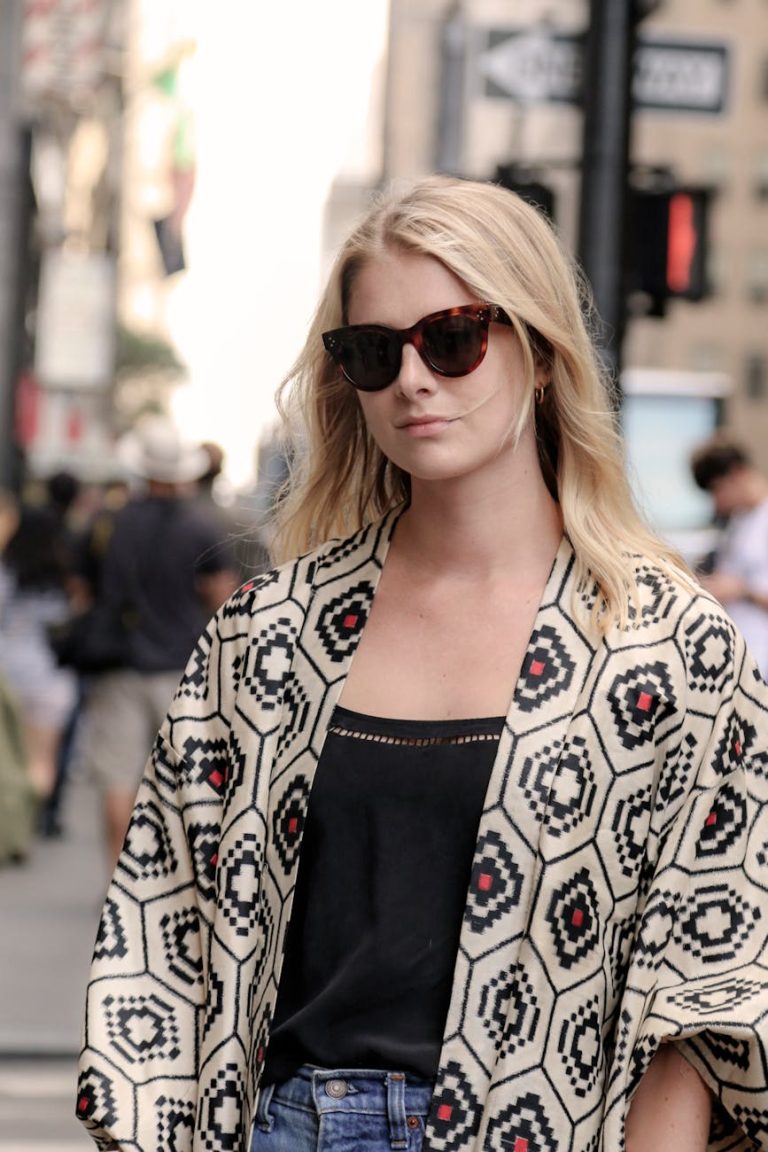 Stylish woman wearing sunglasses and patterned coat on a busy New York City street.