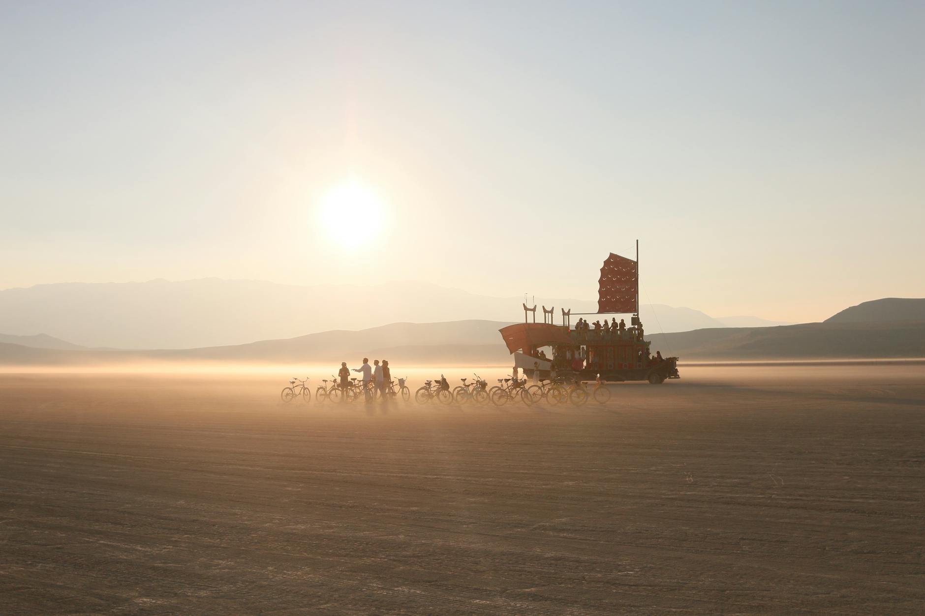 Bikers ride alongside a unique art car at sunrise in the Nevada desert.
