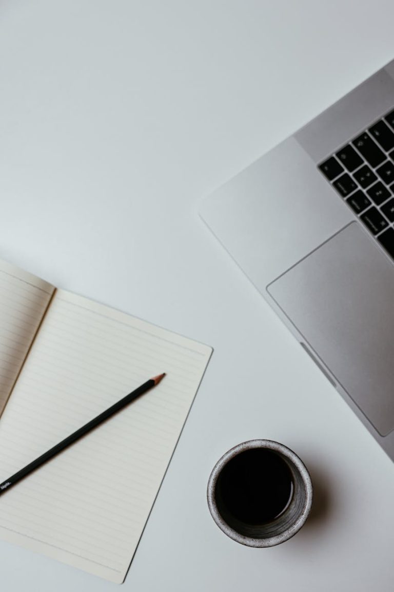 A clean, minimalist desk setup featuring a laptop, notebook, and coffee cup for productive work.