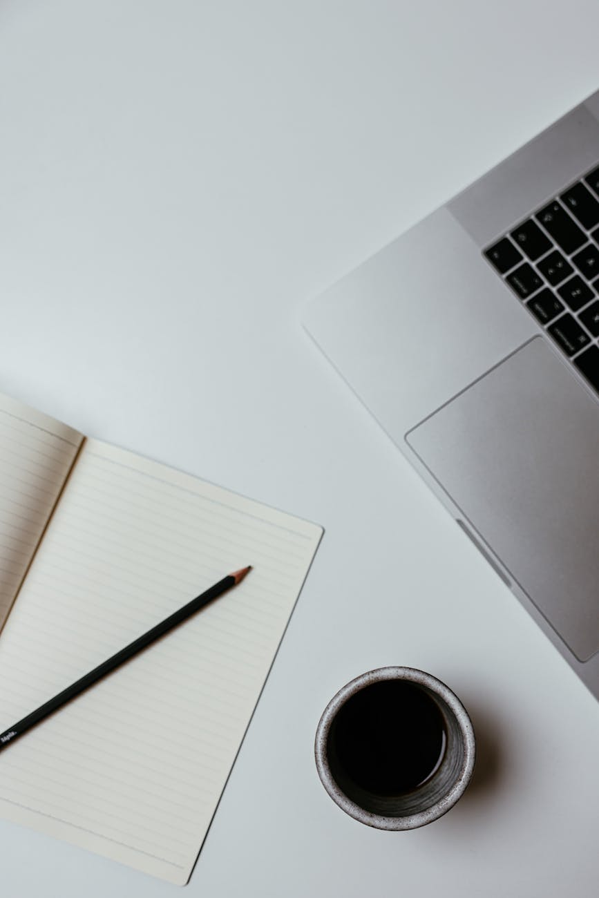 A clean, minimalist desk setup featuring a laptop, notebook, and coffee cup for productive work.