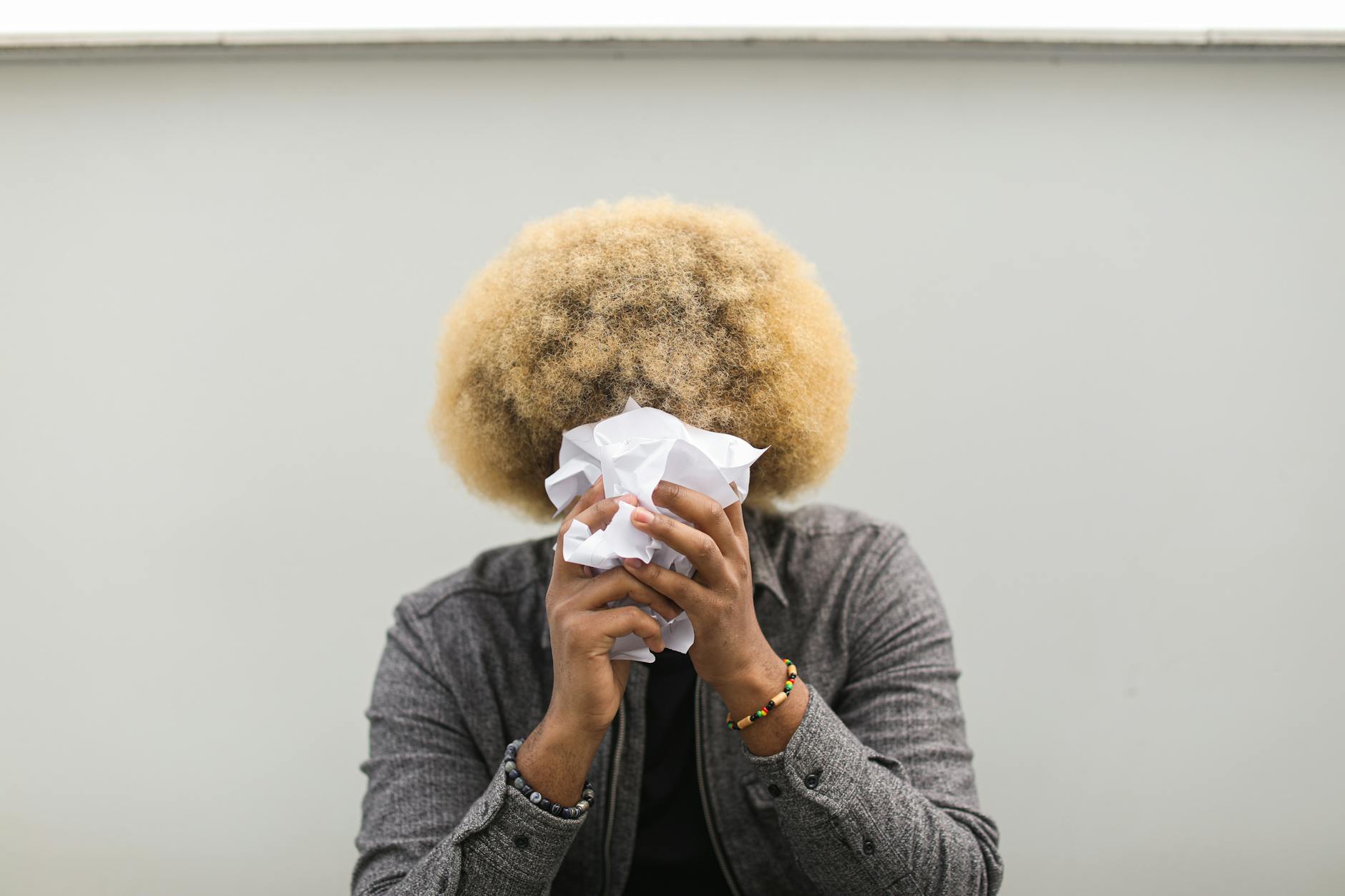 A person with afro hair hides face with crumpled paper, showing creativity and introspection.