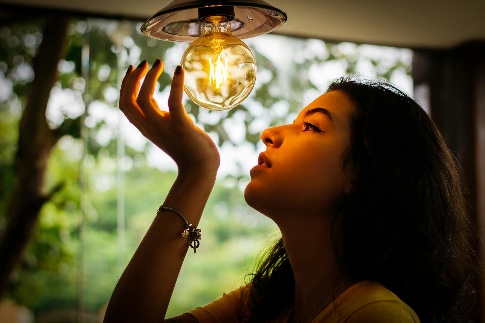 A dramatic portrait of a woman reaching towards an illuminated light bulb indoors.