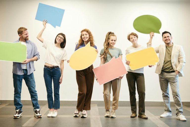 Diverse group of smiling adults holding vibrant speech bubbles indoors.