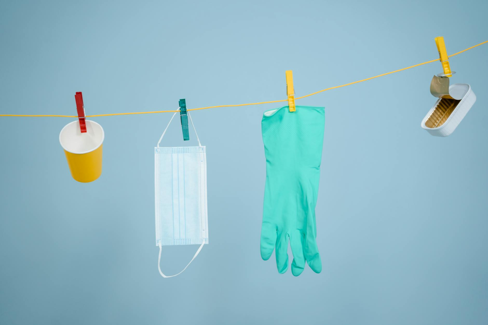 Various recyclable items like glove, mask, and can hanging on a clothesline.