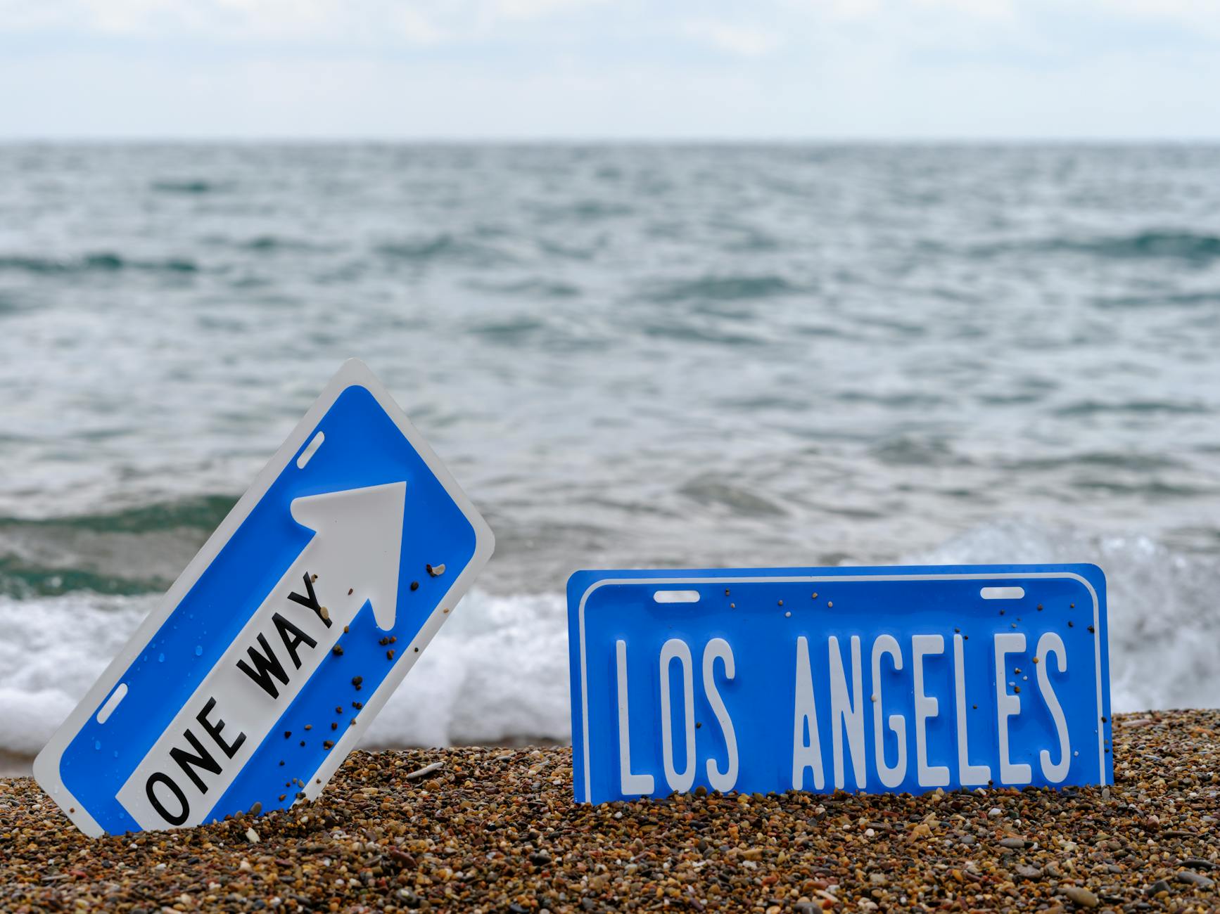 Ocean view with Los Angeles and one way signs placed on a sandy beach.
