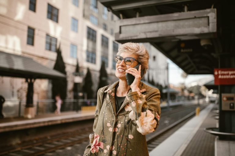 Elderly woman enjoying a phone call while waiting at an urban train station platform.