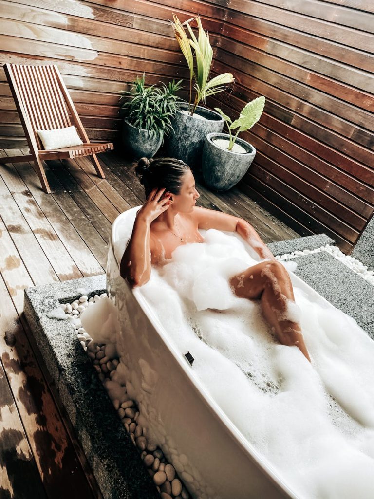 Woman relaxing in a foam-filled bathtub in a stylish outdoor setting at a resort.