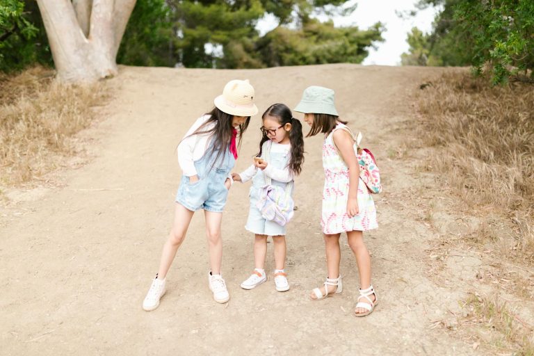 Three young girls having fun outdoors, showcasing friendship and discovery on a dirt path.