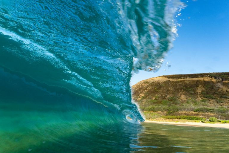 Captivating image of a powerful ocean wave curling near a rocky coastline under clear skies.