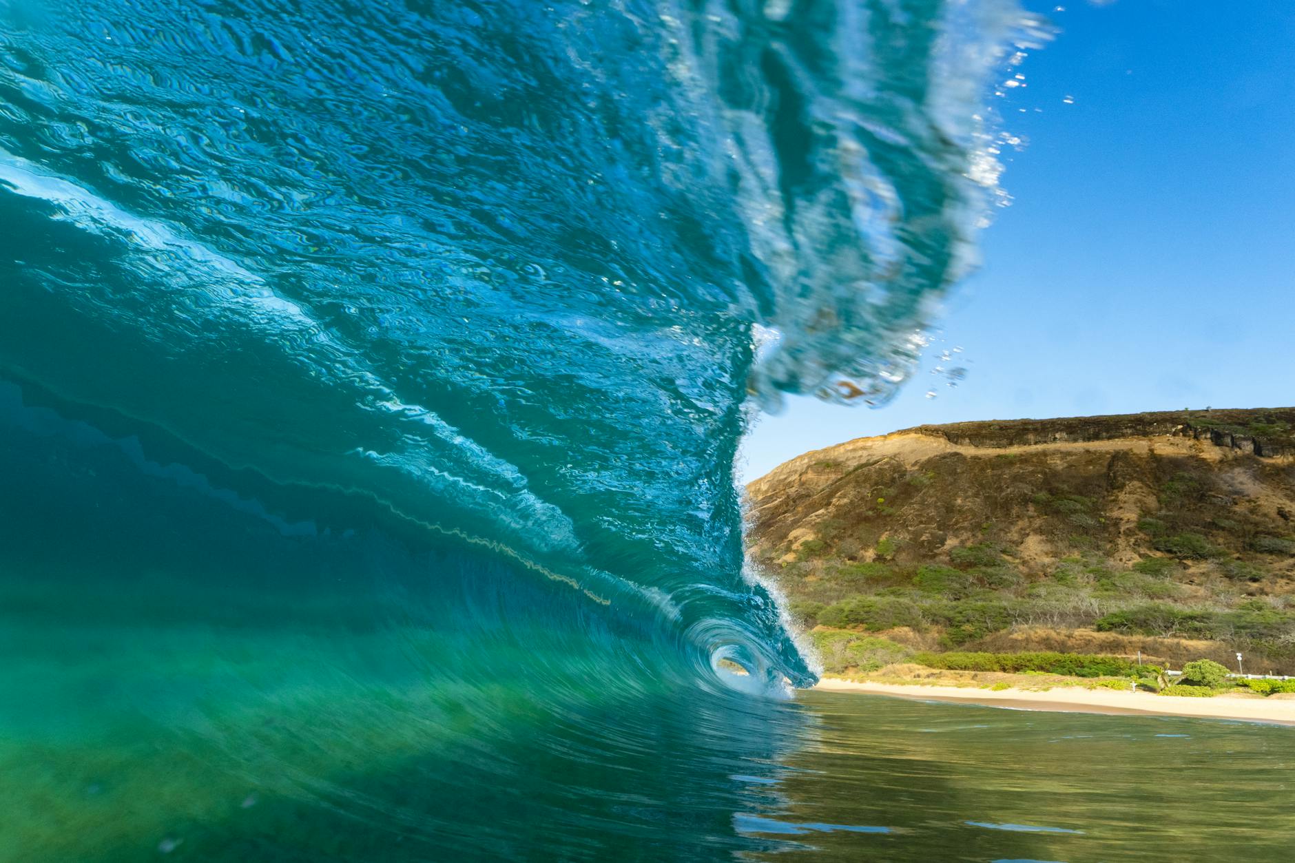 Captivating image of a powerful ocean wave curling near a rocky coastline under clear skies.